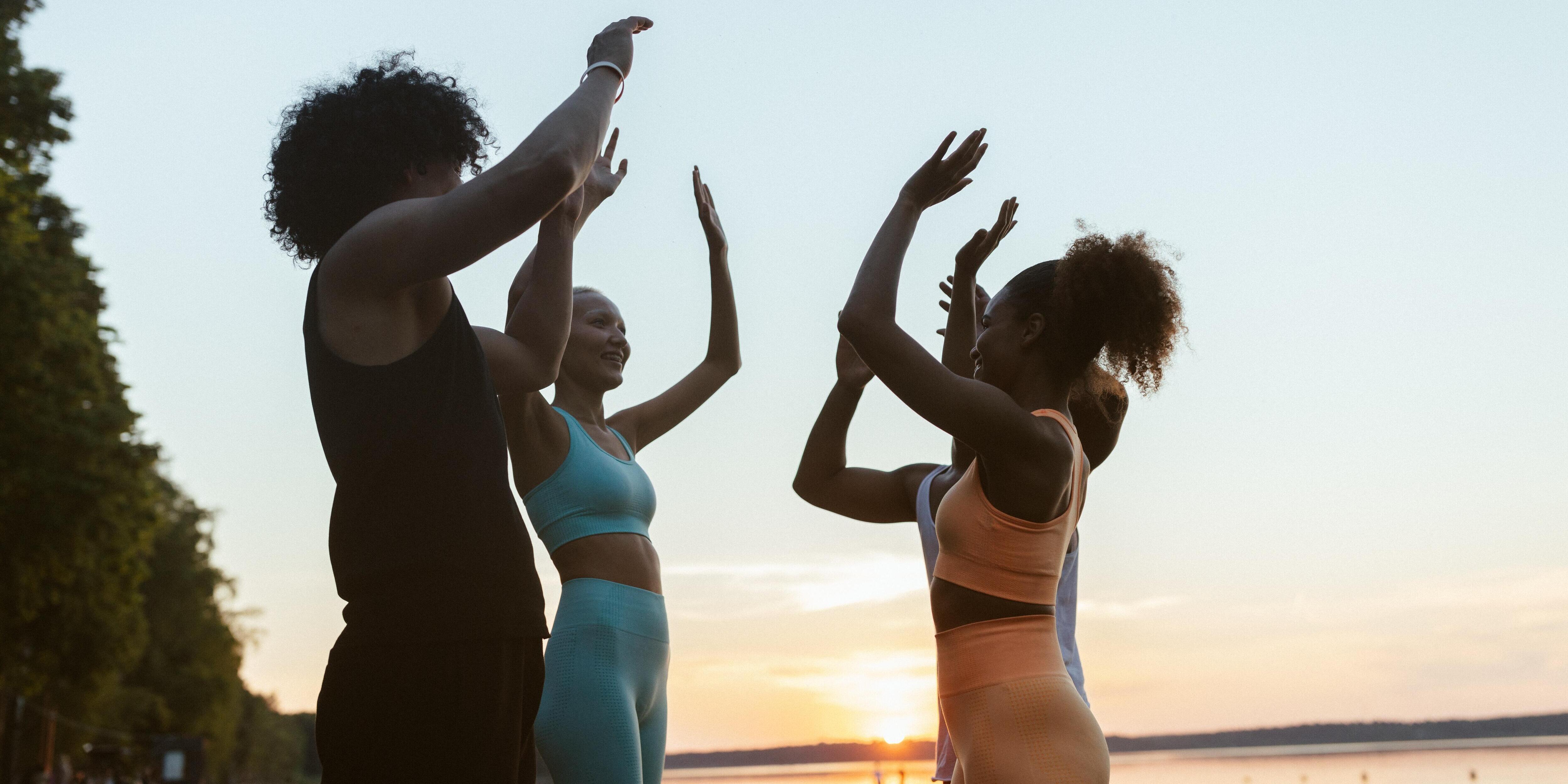 Friends reaching for the sunrise sky in athletic clothes