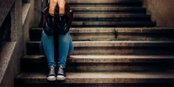 Lone person sitting on deserted steps with elbows on knees and hands covering face