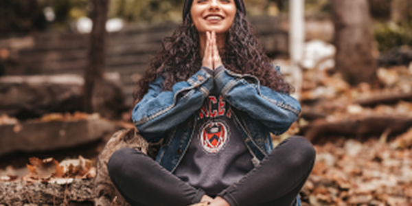 Happy young woman sitting cross-legged on forest floor with hands together in meditation